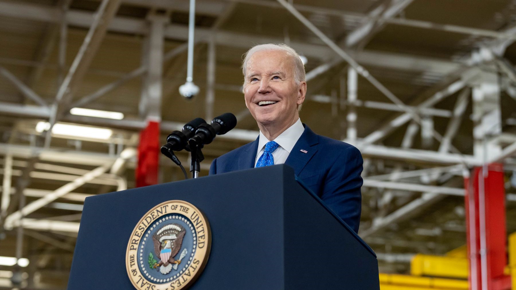 President Biden smiling at a crowd while standing at a podium.