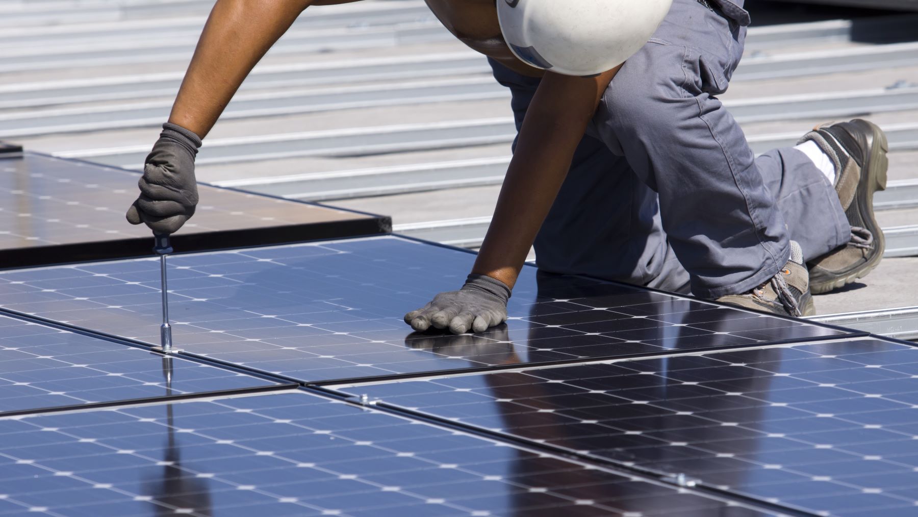 Person kneeling over a solar panel and screwing a part in.