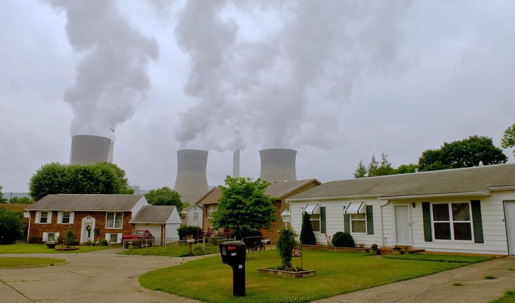 Cooling towers of a coal-fired power plant releasing exhaust over a neighborhood.