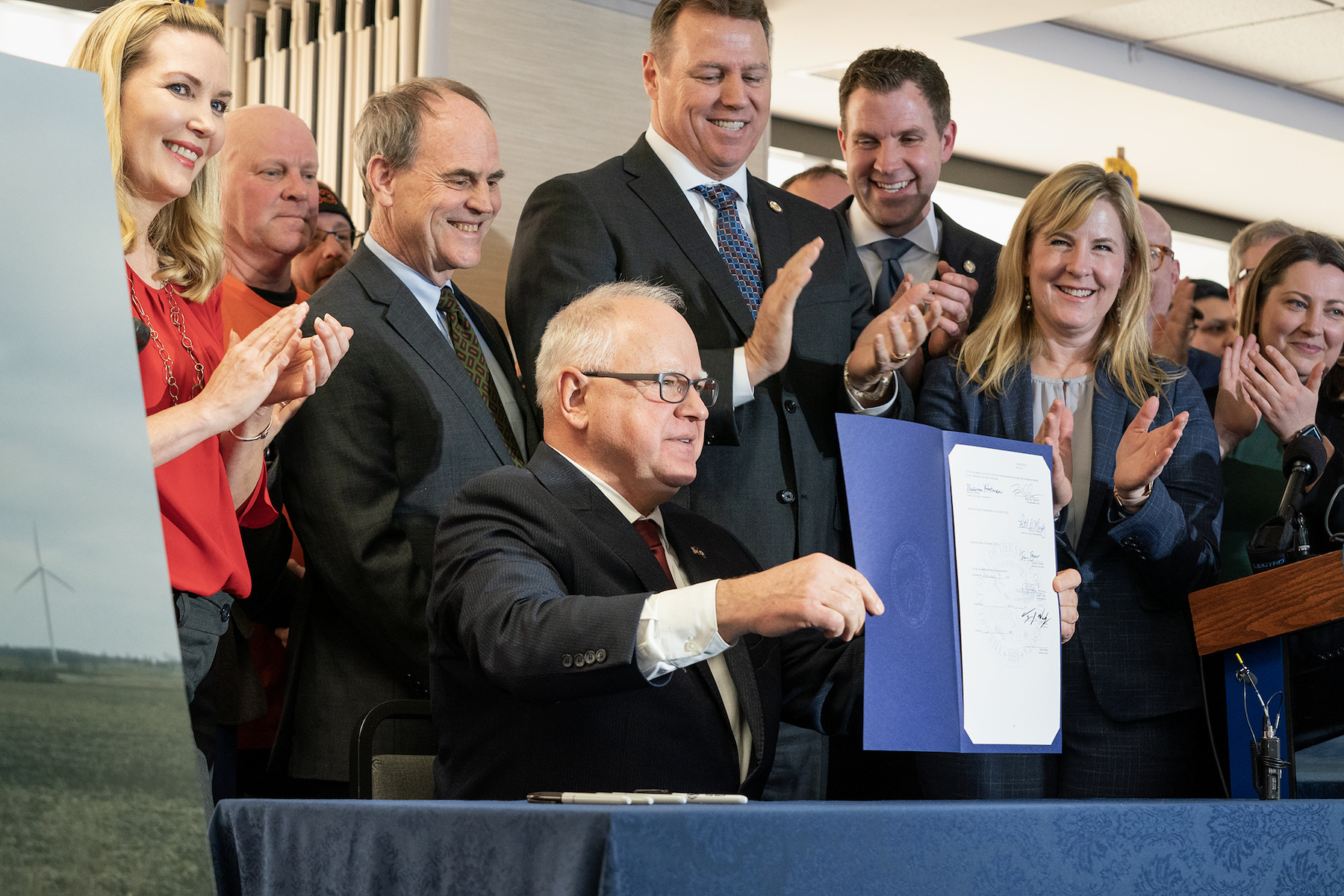 Gov. Tim Walz signs the bill that puts Minnesota on the path to 100 percent clean electricity by 2040. Michael Noble and Rep Jamie Long celebrate behind him.