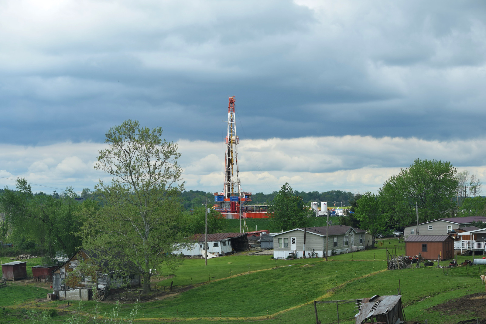 A red and white oil rig seen behind a cluster of small homes on a grassy sloped hill.