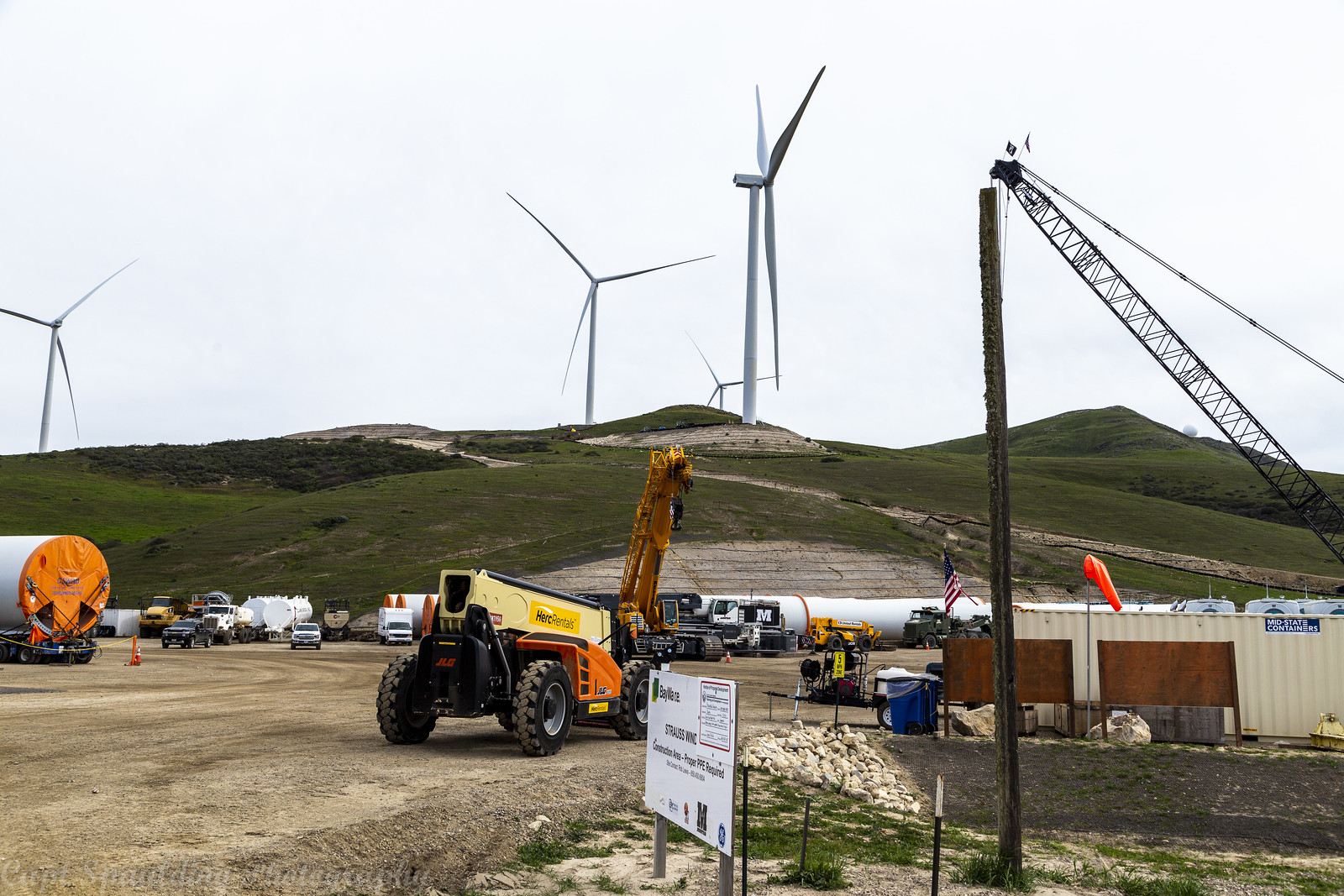 Construction of a wind farm in California. Construction vehicles and equipment seen at the base of the hills where the windmills are.