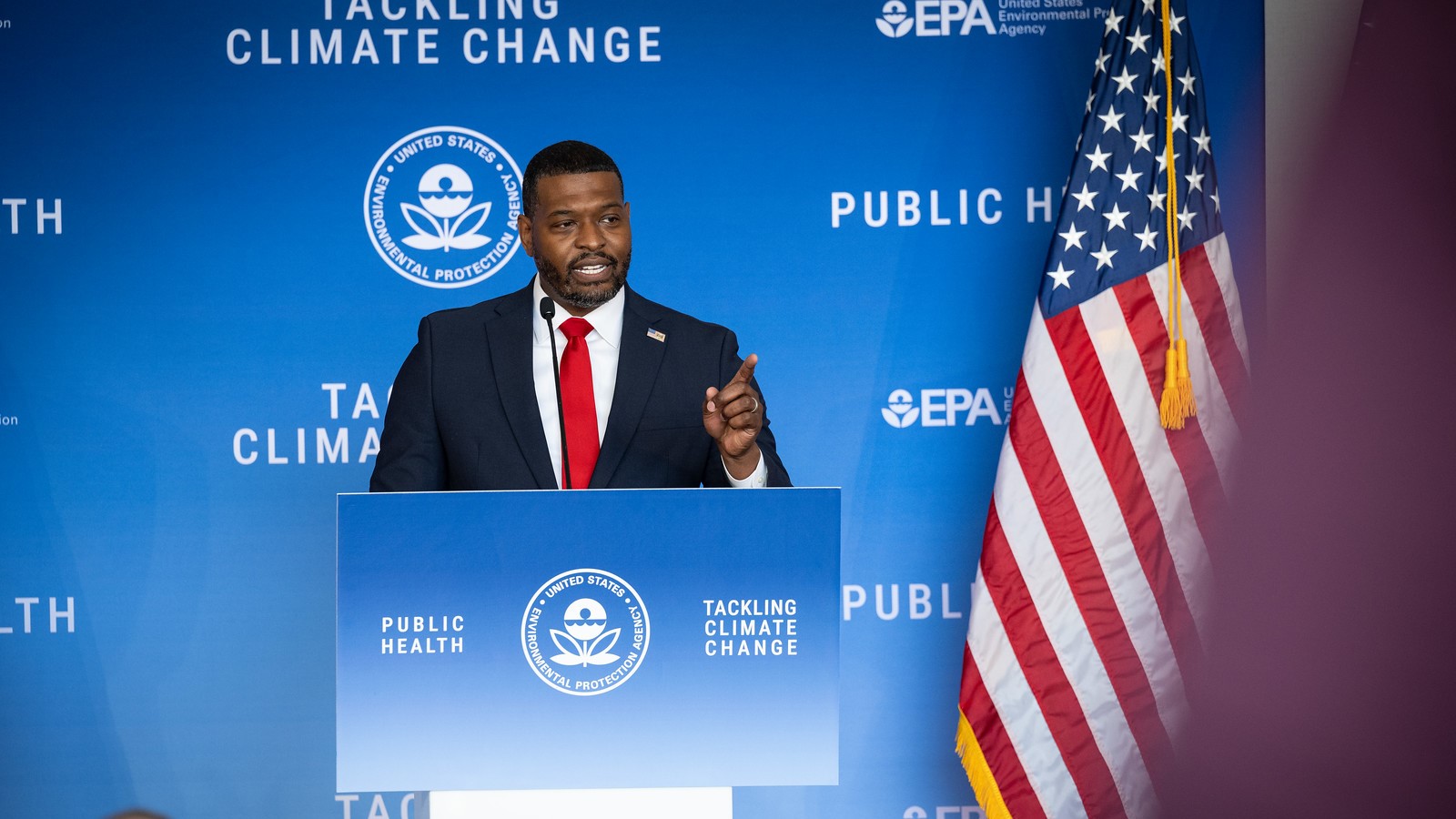 EPA Administrator Michael Regan at a podium announcing EPA's power plant rules. He is standing next to an American flag and is in front of a blue backdrop that says 