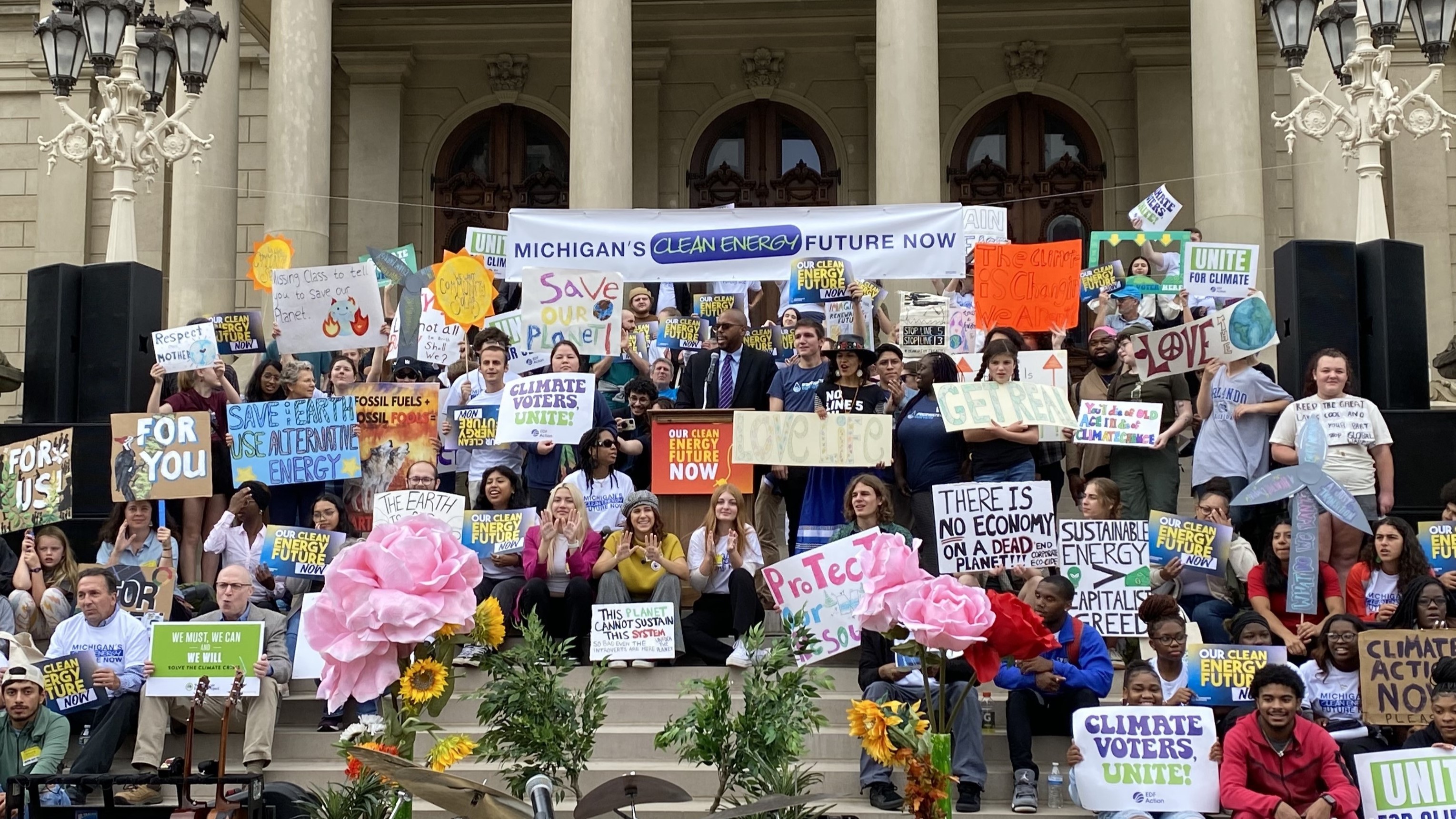 Activists holding pro-climate action signs on the steps of the Michigan capitol building.