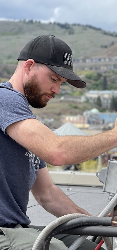 A man installs a ductless heat pump on a roof